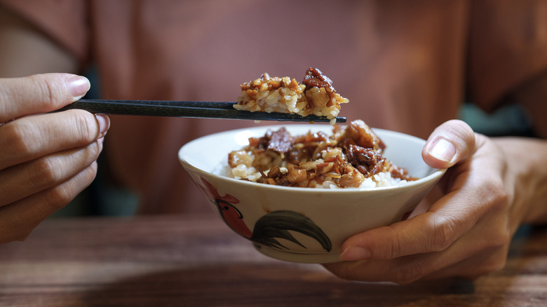 woman holding bowl of rice and meat with chopsticks in hand