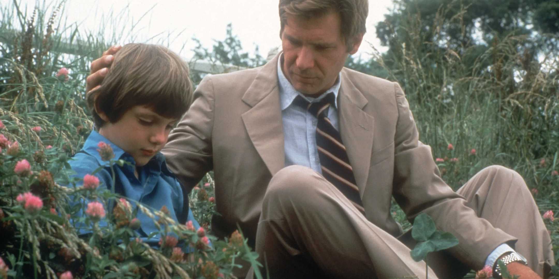 Harrison Ford as John Book sitting next to a boy in a field in Witness