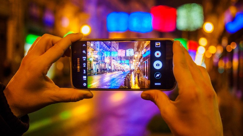 A person taking a photo of a city street at night using a Samsung phone.