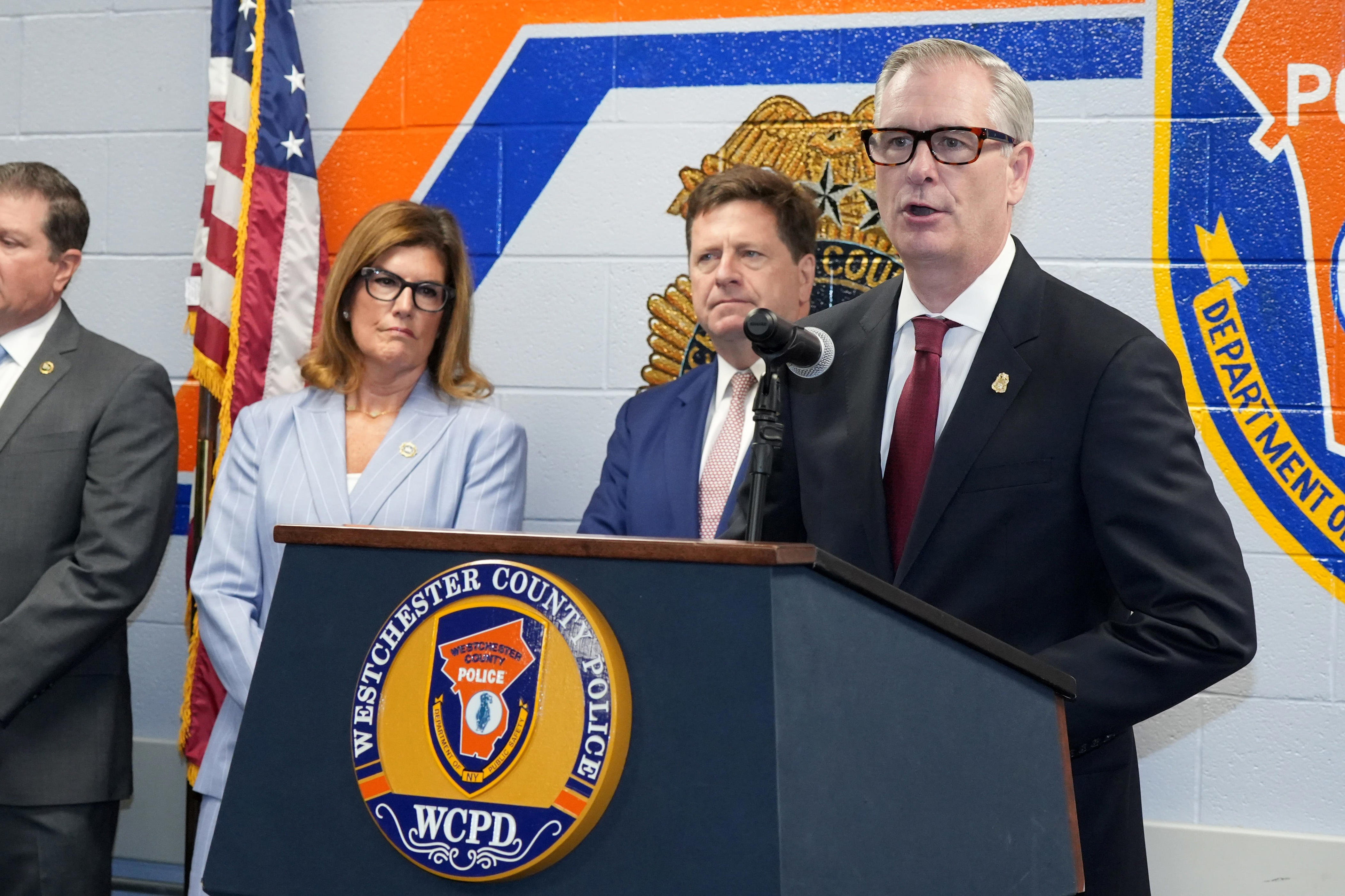 James Barnacle, assistant director in charge of the FBI New York Field Office, joins Westchester District Attorney Susan Cacace and U.S. Attorney Jay Clayton to announce charges against 11 members of a Trinitarios street gang in a 15-count indictment involving five murders July 20, 2026 at Westchester Police Academy in Valhalla. The indictment solved the fatal Cross County Parkway shooting of social media influencer Ariela La Langosta and four other murders in the New York metropolitan area.