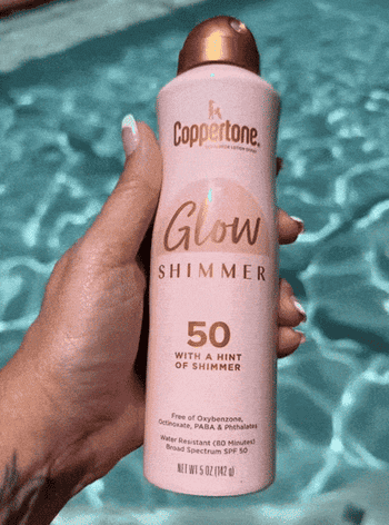 Hand holding a Coppertone Glow Shimmer SPF 50 sunscreen bottle with a pool in the background