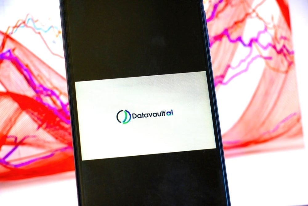 DataVaultAI logo displayed in foreground on mobile phone with stock chart in background on computer screen
