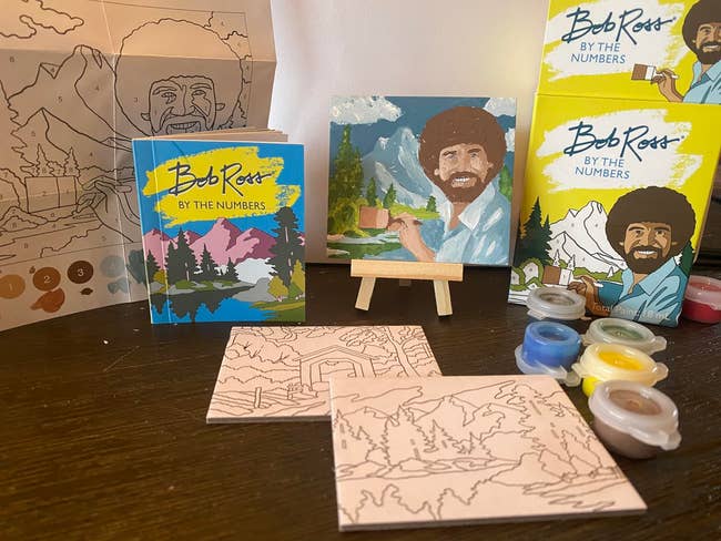 Bob Ross painting kit includes paint pots, brushes, canvases, and a mini easel, ideal for art enthusiasts looking to recreate nature scenes