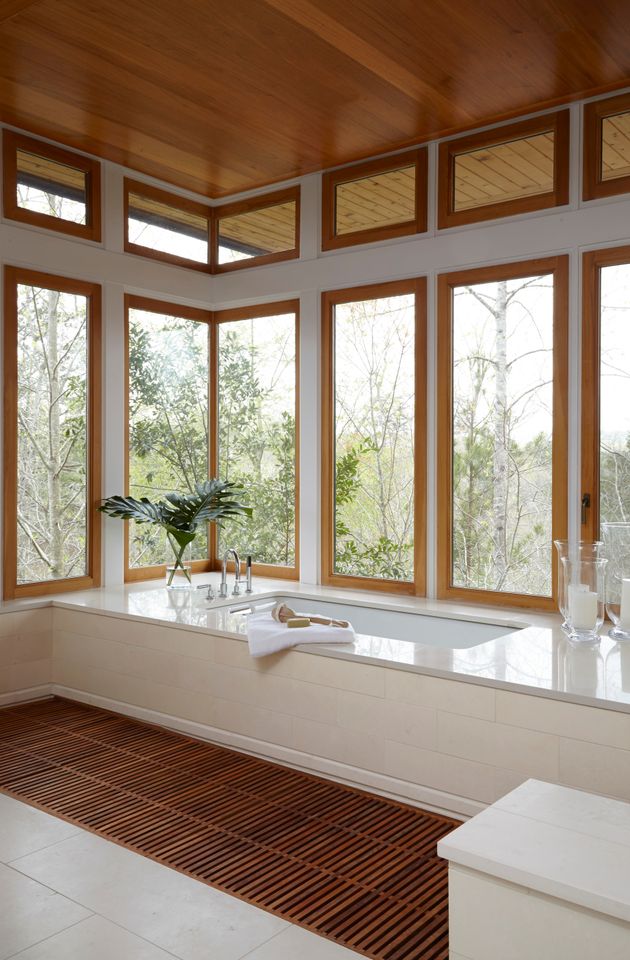 A modern bathroom interior featuring a large bathtub surrounded by large windows with a natural outside view