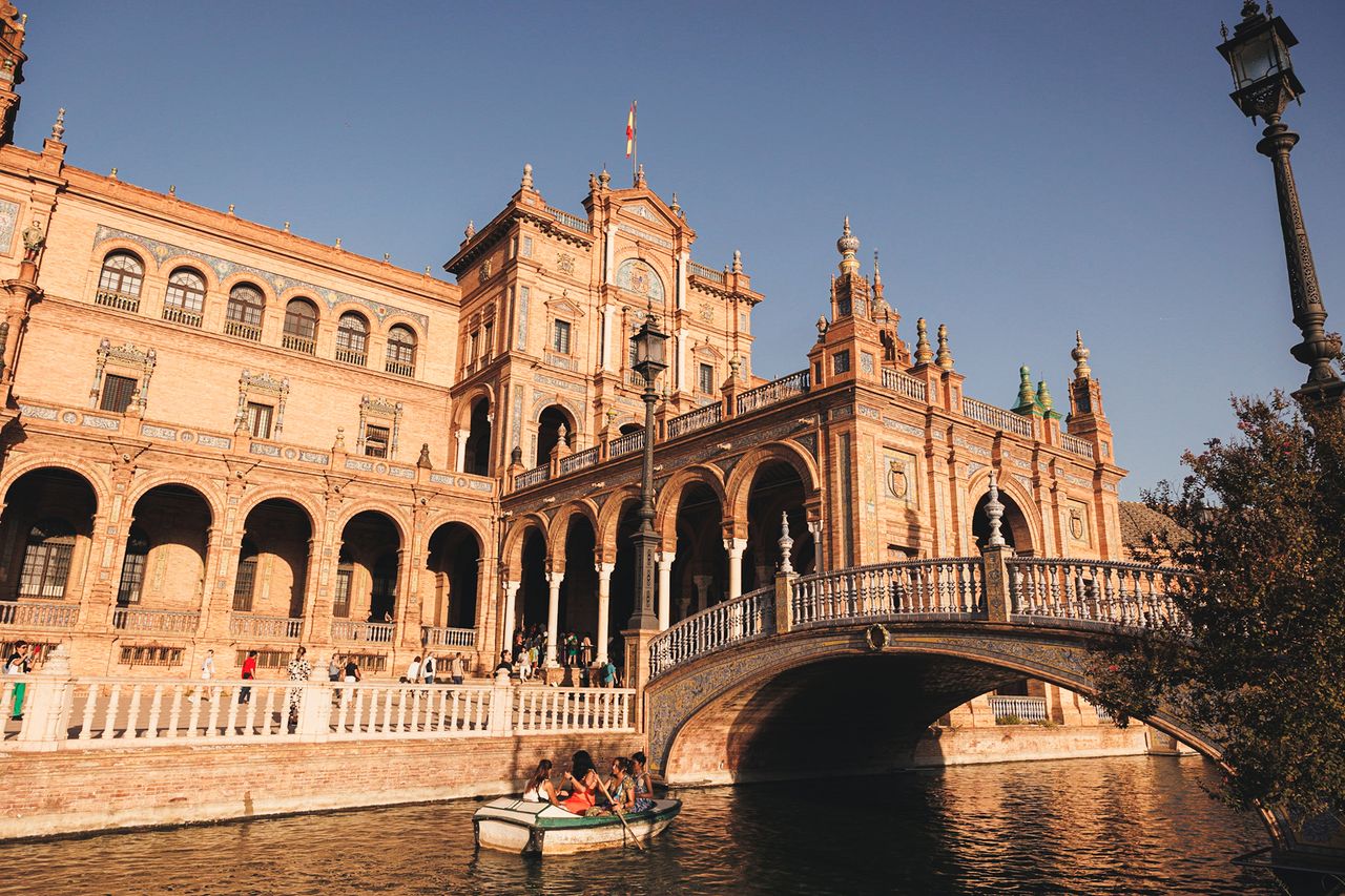 Plaza de Espaa in Seville with bridge and canal featuring architecture and visitors on a boat in the foreground