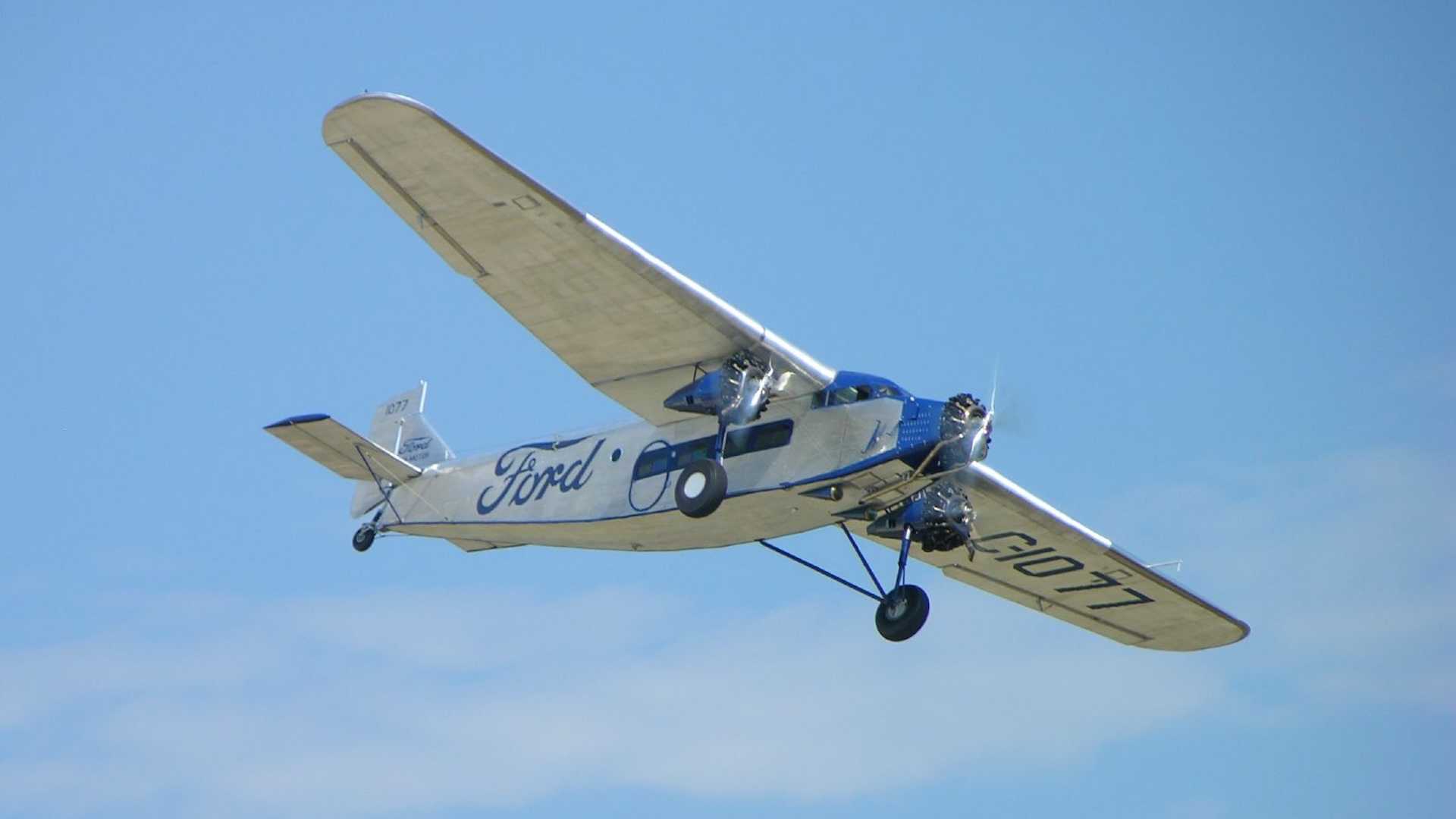 Silver airplane with a Ford logo on the side, a blue sky in the background.