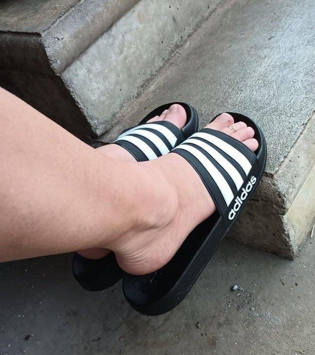 Person wearing black and white striped Adidas slides, sitting on a concrete step