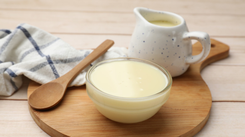 A bowl of condensed milk with a creamer jar and a wooden spoon