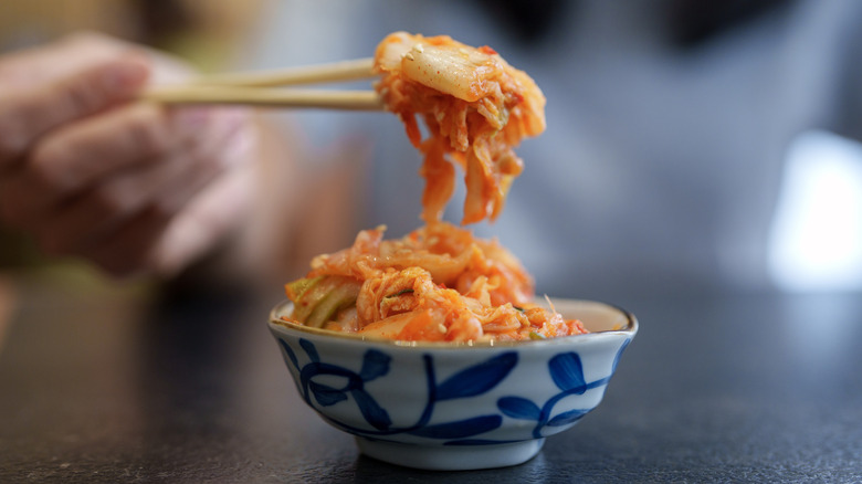 Person using chopsticks to take a piece of kimchi from a bowl