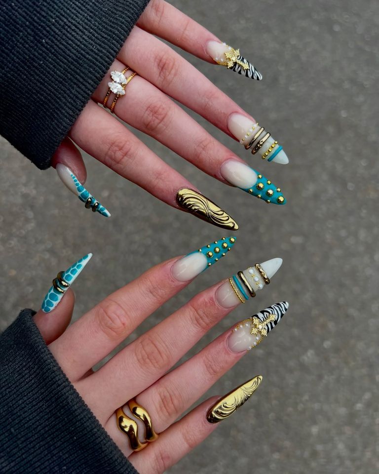 Manicured hands with long decorative nails featuring detailed designs and rings on fingers