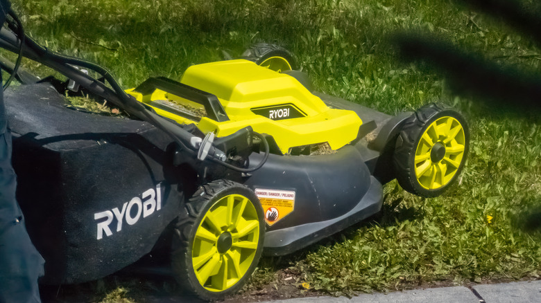 A Ryobi electric lawn mower running over grass.
