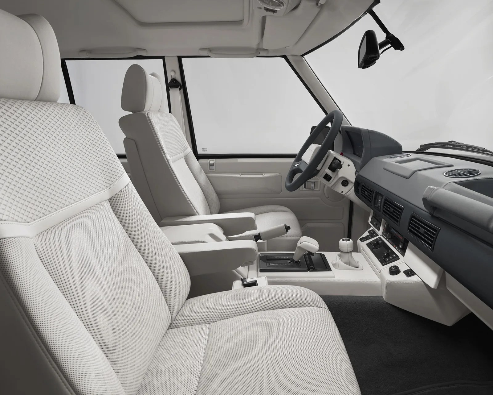 Light gray fabric front seats and armrests inside a vehicle with a black and white dashboard and steering wheel.