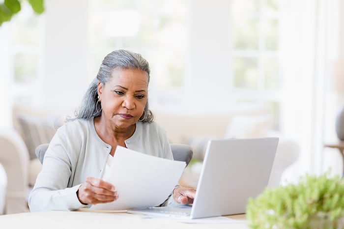 Serious person looking at document and typing on laptop.