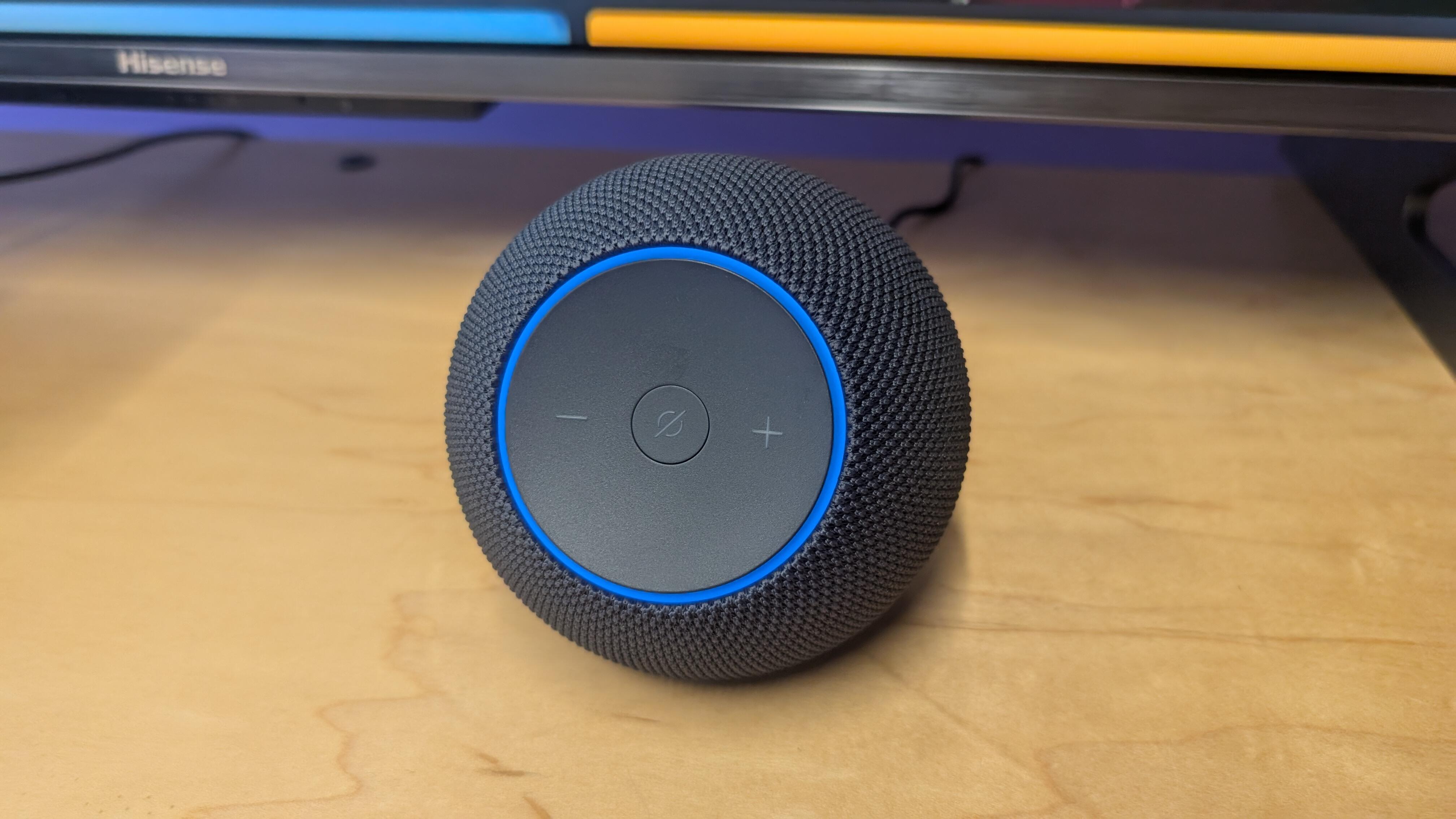 A black Amazon Echo Studio sits on a wooden desk.