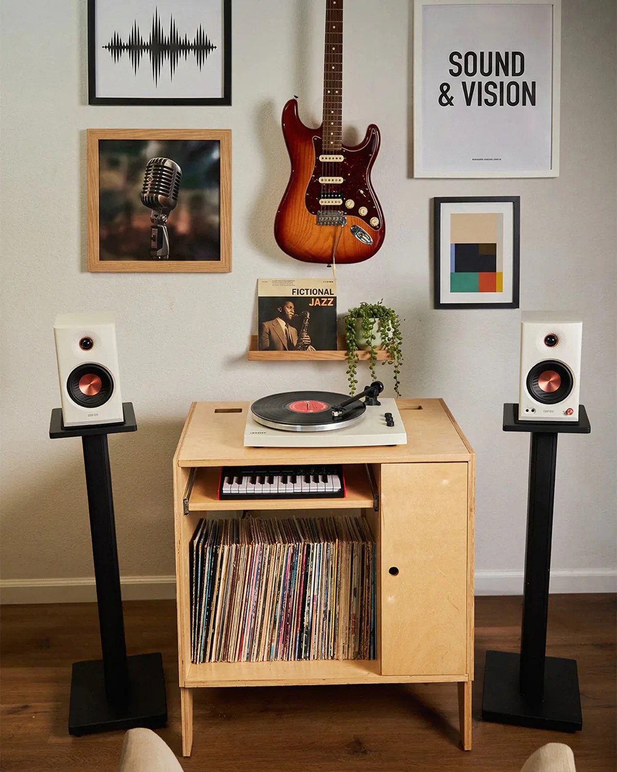 Wooden record cabinet with vinyl collection, white turntable, two white speakers on black stands, and a sunburst electric guitar hanging above.