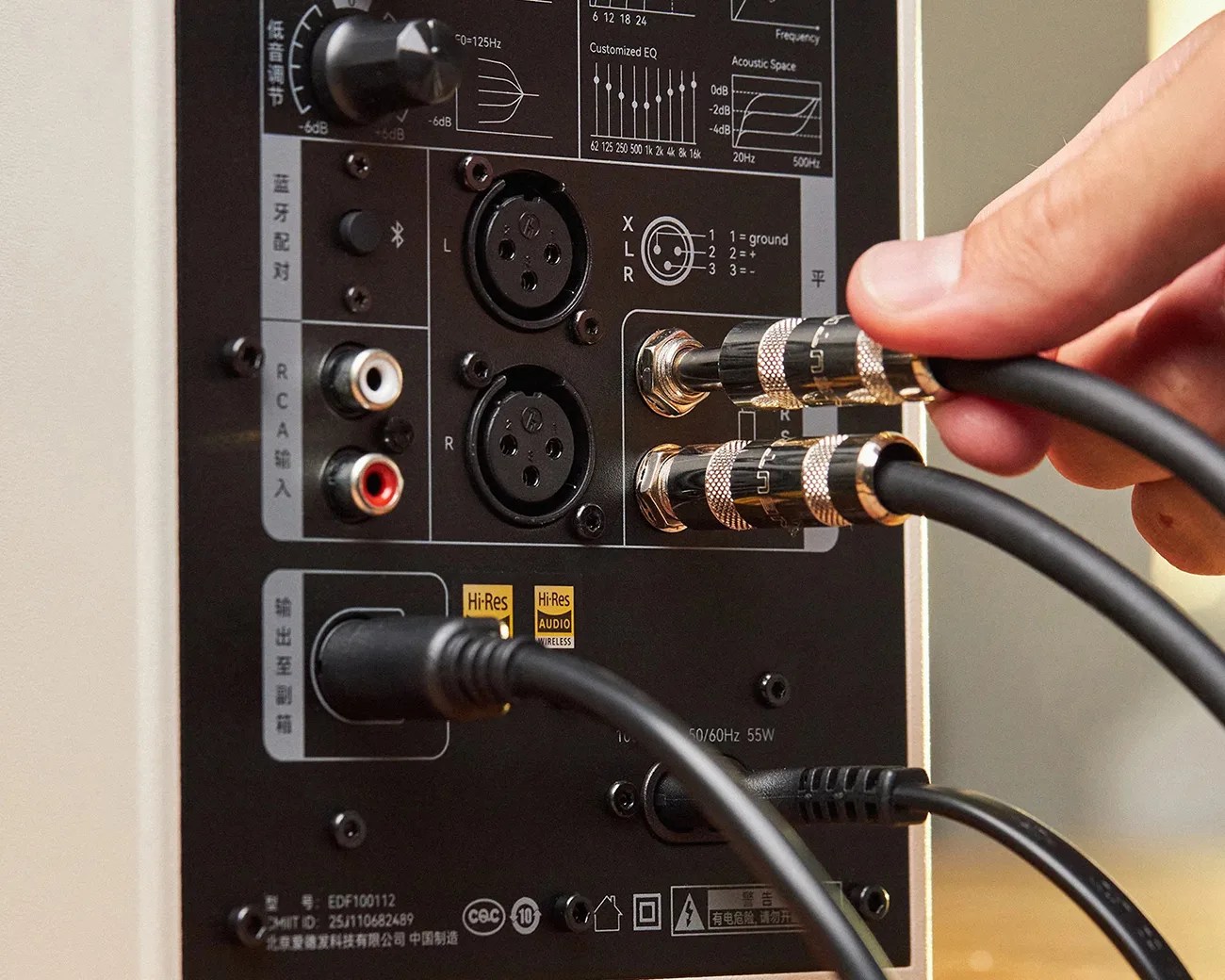 Close-up of a hand plugging black audio cables into gold-plated connectors on a black audio device panel with various input ports.