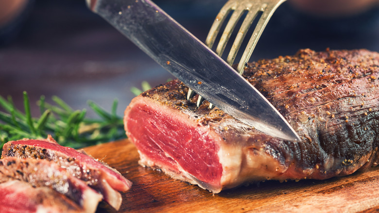 Hands cutting medium roasted beef steak on the wooden board