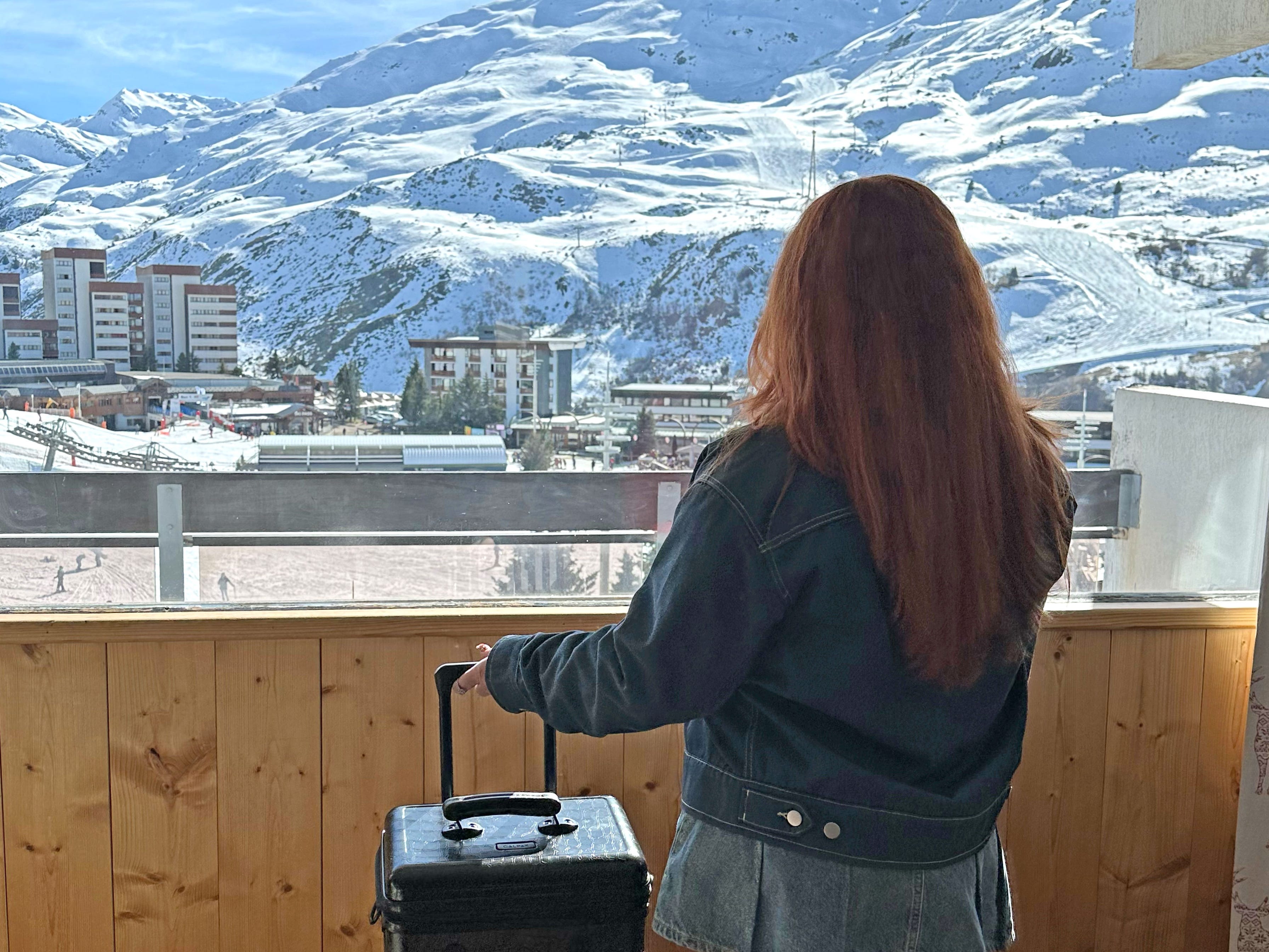 Annmarie's hand is on her suitcase handle as she looks out at the snowy French Alps.