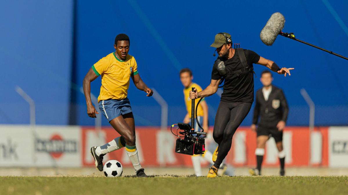 A camera crew captures soccer action for the series Brazil '70: The Third Star. A cameraman captures a soccer player with others in the background.