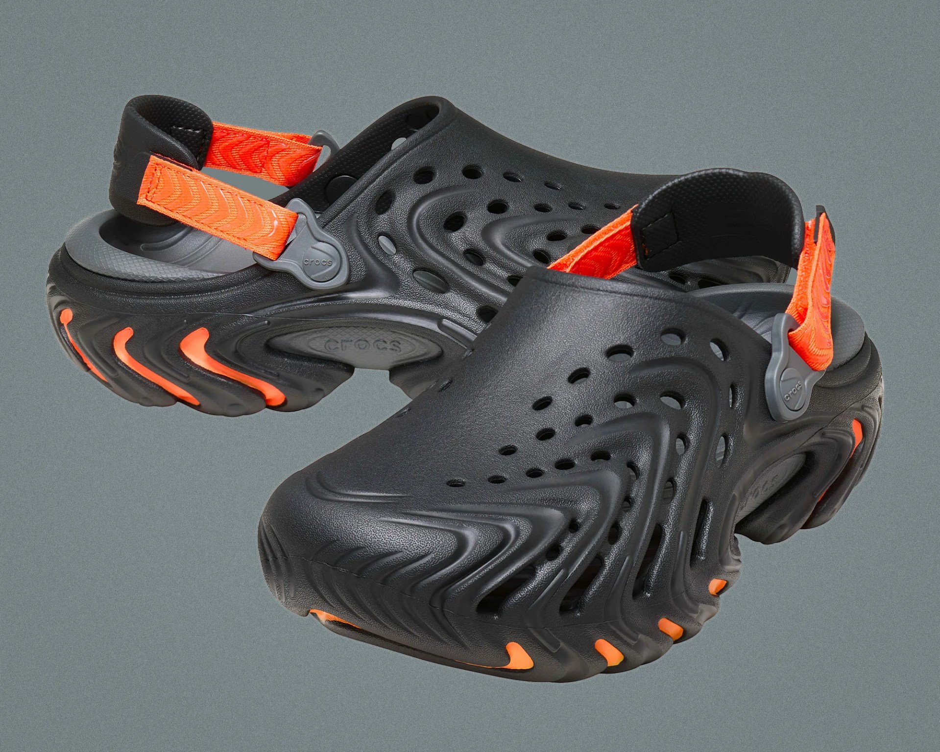 Black Crocs with textured surface, ventilation holes, and bright orange adjustable heel straps and sole accents.