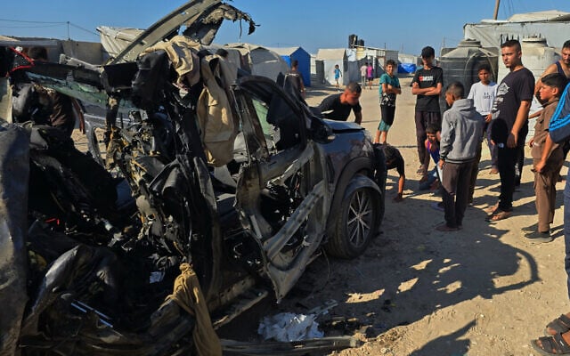 Palestinians look at a destroyed car following an Israeli military strike that, according to hospital officials, killed at least three people in Khan Younis, southern Gaza Strip, July 20, 2026. (Mohammad Jahjouh/AP)