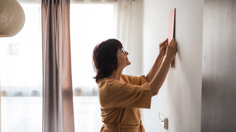 A woman mounting a picture on the wall holding it against the surface.