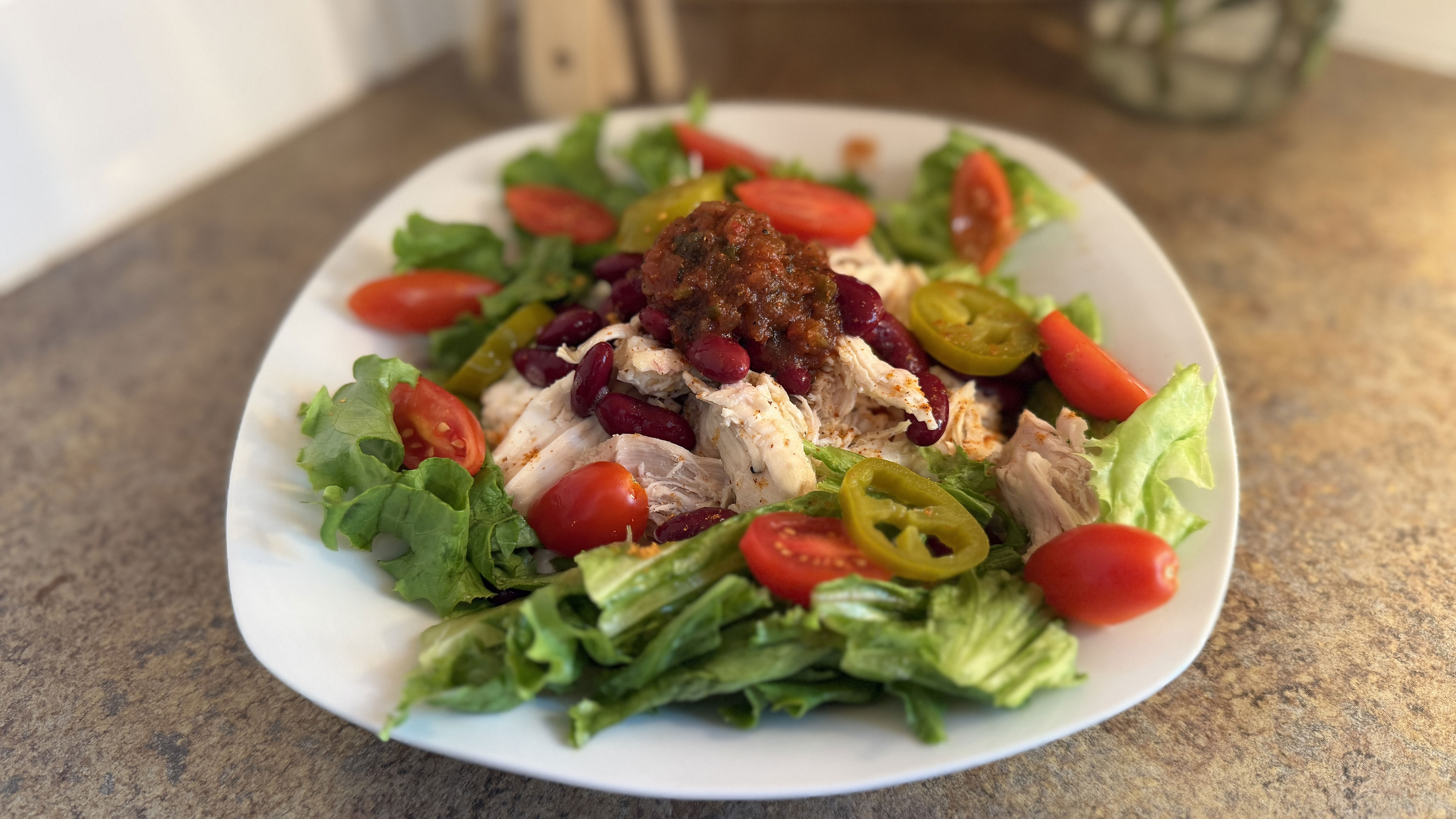 Plate of salad, with bed of lettuce topped with ingredients including cherry tomatoes, chicken, and jalapeños