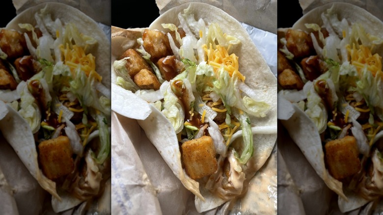 Taco Bell Spicy potato soft taco open with the sauce, lettuce, and cheese inside on top of the spiced potato chunks