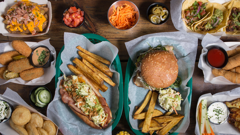 A variety of food including a submarine sandwich, french fries, hamburger, tacos, jalapeno poppers, chicken wings and more
