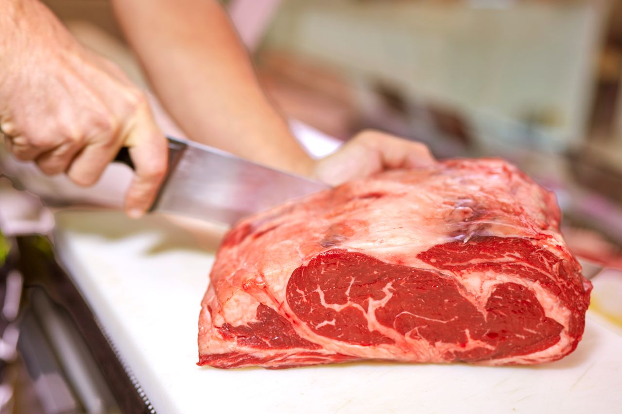 A person slicing a large piece of raw steak with a knife on a cutting board
