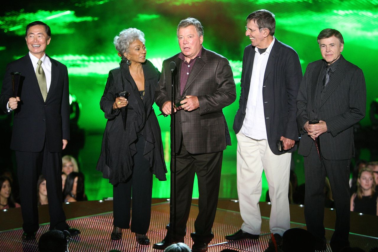 William Shatner George Takei and Walter Koenig standing together on stage with other individuals