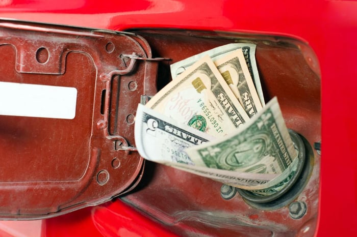 US dollar bills stuffed into a red car’s gas tank, symbolizing high fuel costs