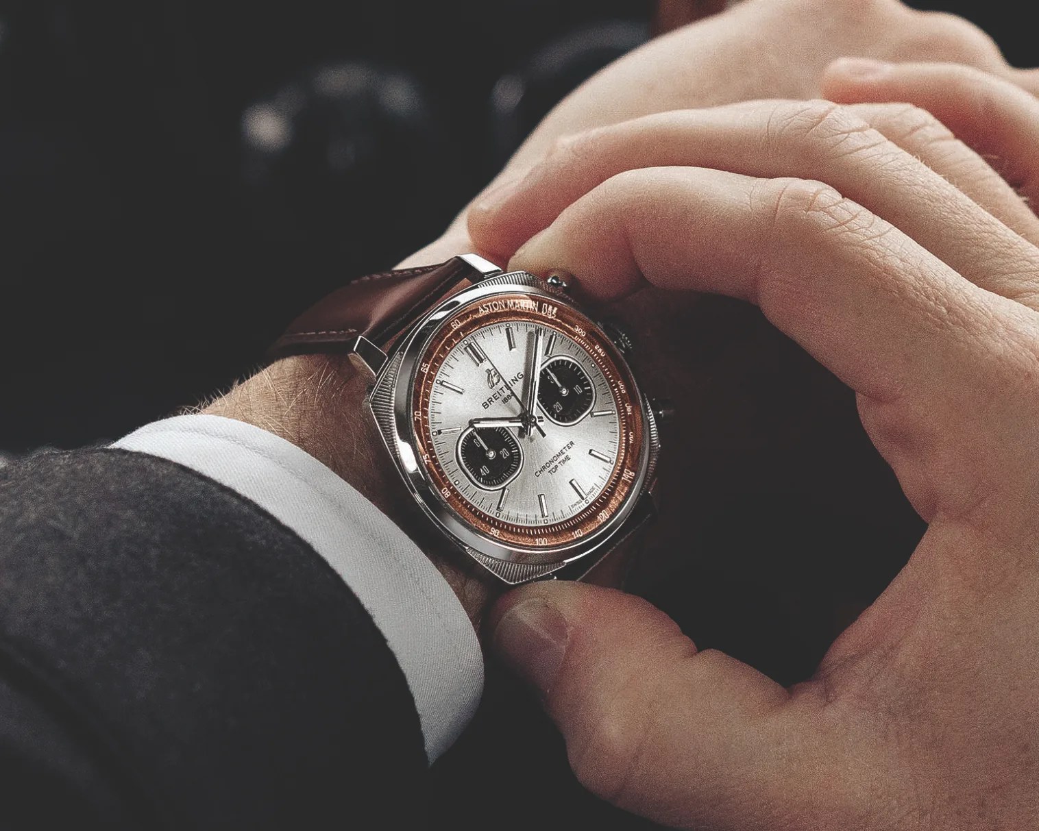 Silver Breitling chronometer wristwatch with brown leather strap worn on a wrist, adjusted by a hand.