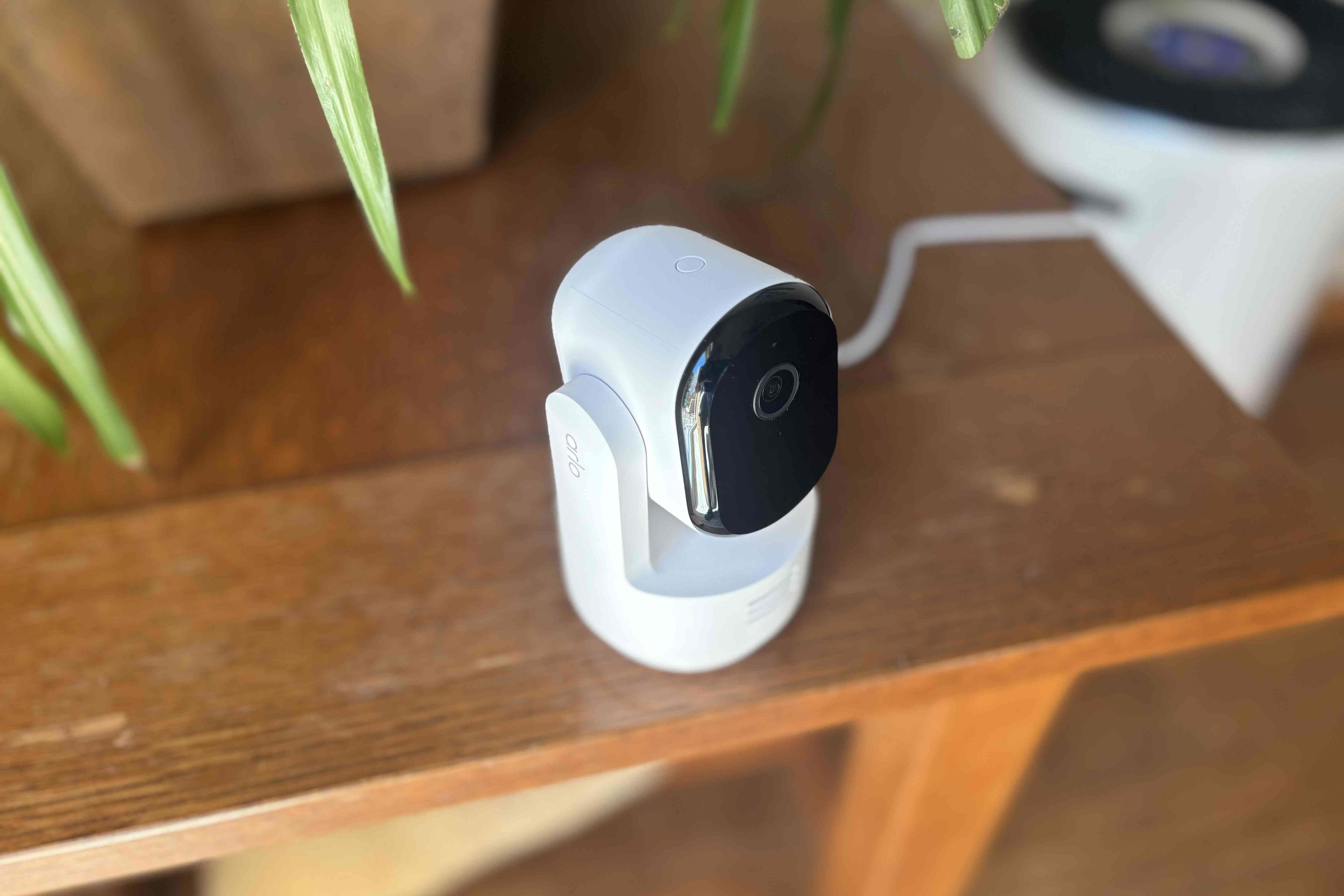 Arlo's pan/tilt white camera on a wood table corner.
