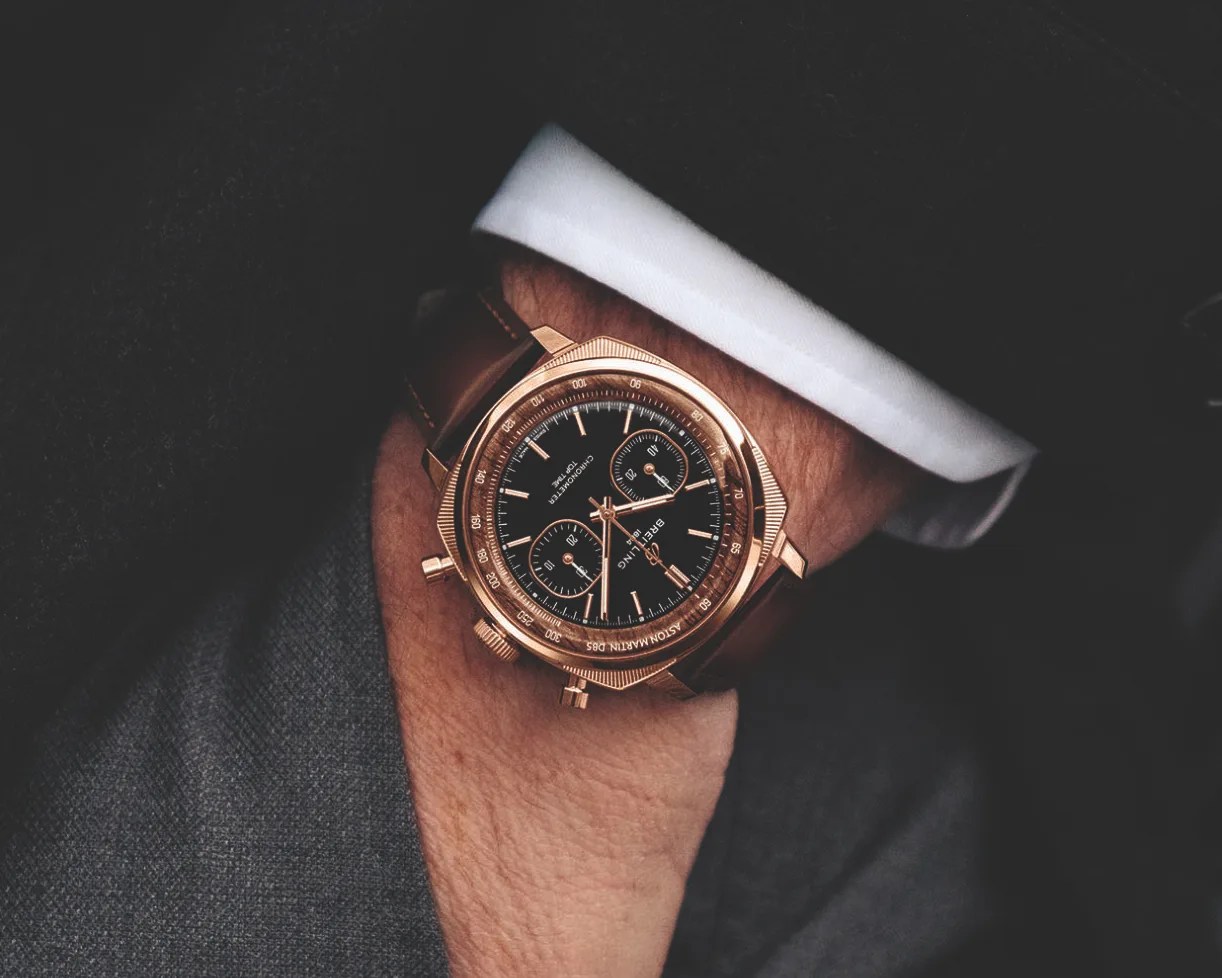 Rose gold Breitling chronograph watch with black dial and brown leather strap worn on a wrist.