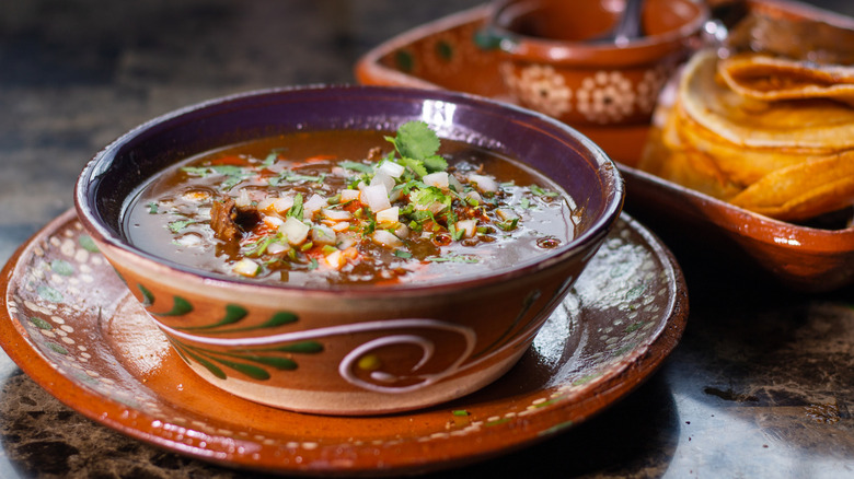 Traditional Mexican dish with beef birria with red sauce in a decorative terra cotta bowl garnished with onions and cilantro