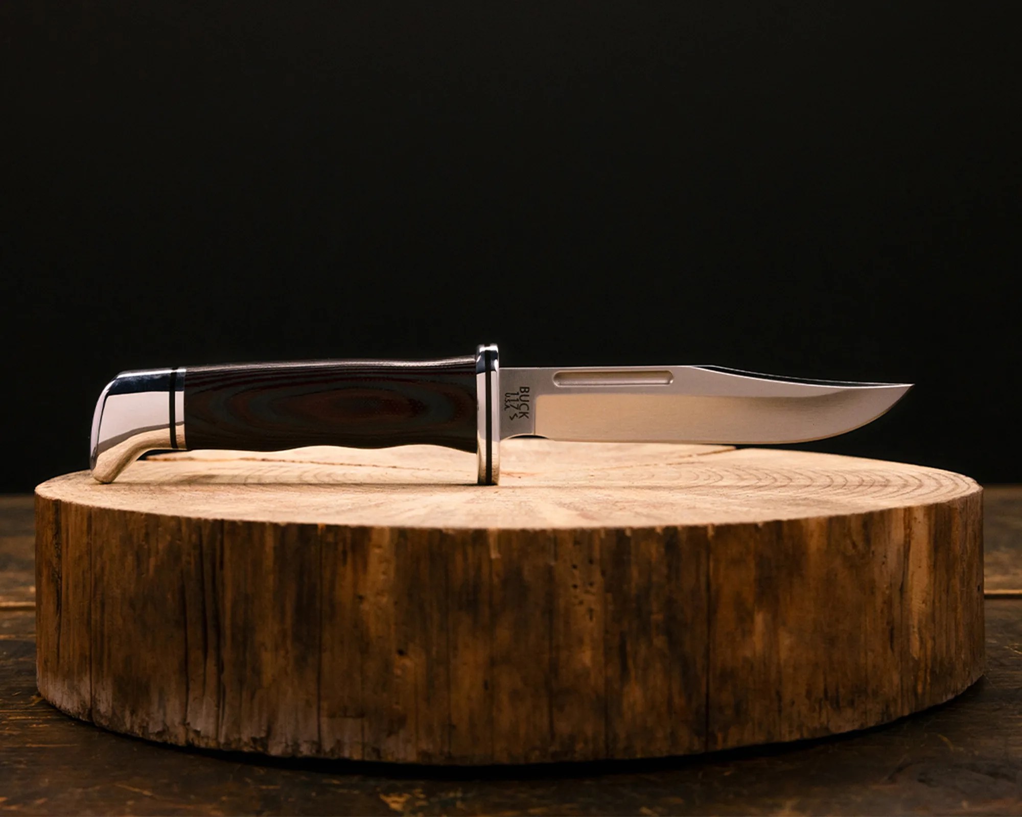 Fixed-blade knife with a polished metal blade and dark wooden handle resting on a round wooden surface.