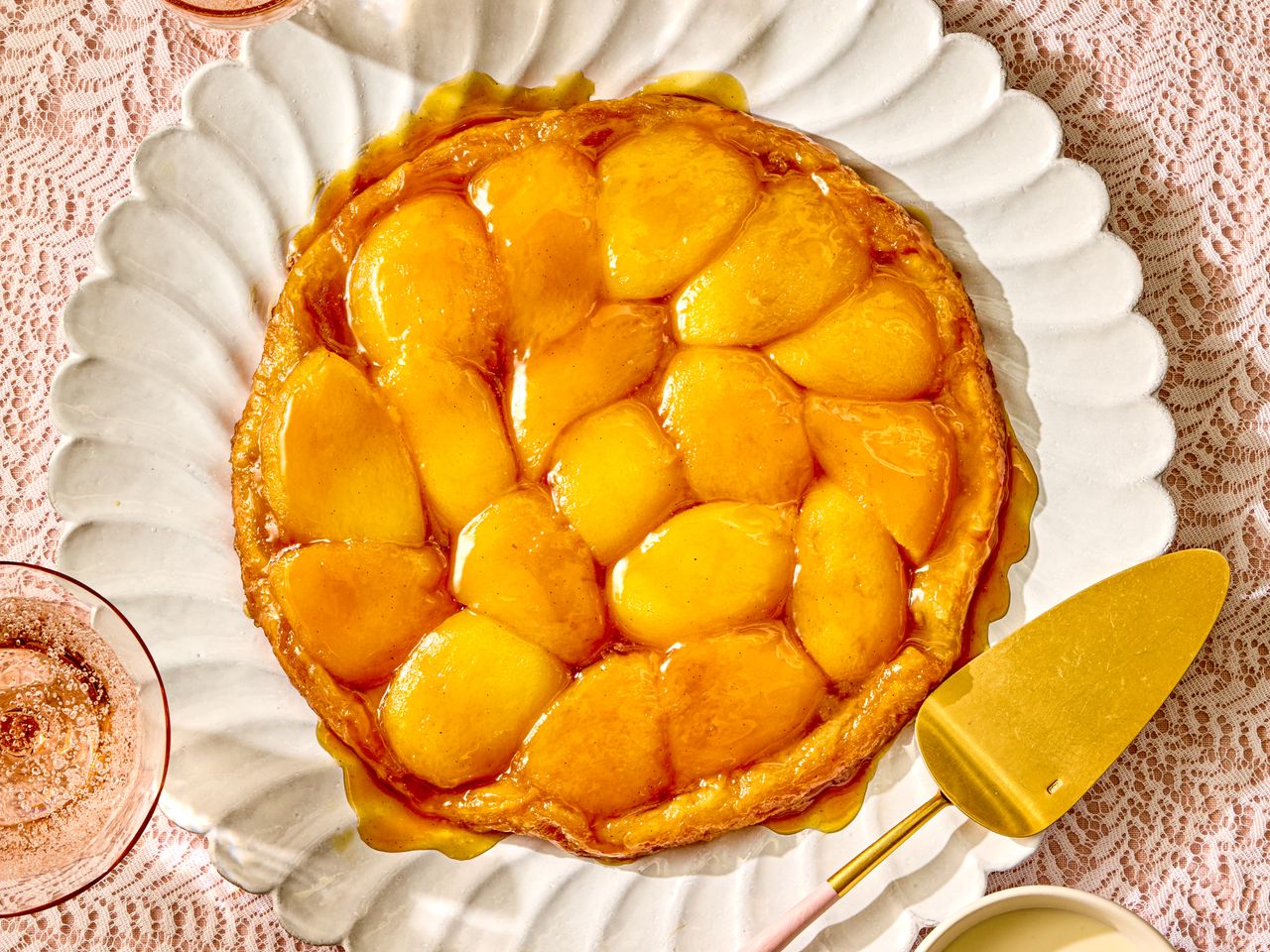A peach tarte tatin on a decorative plate with a serving utensil beside it