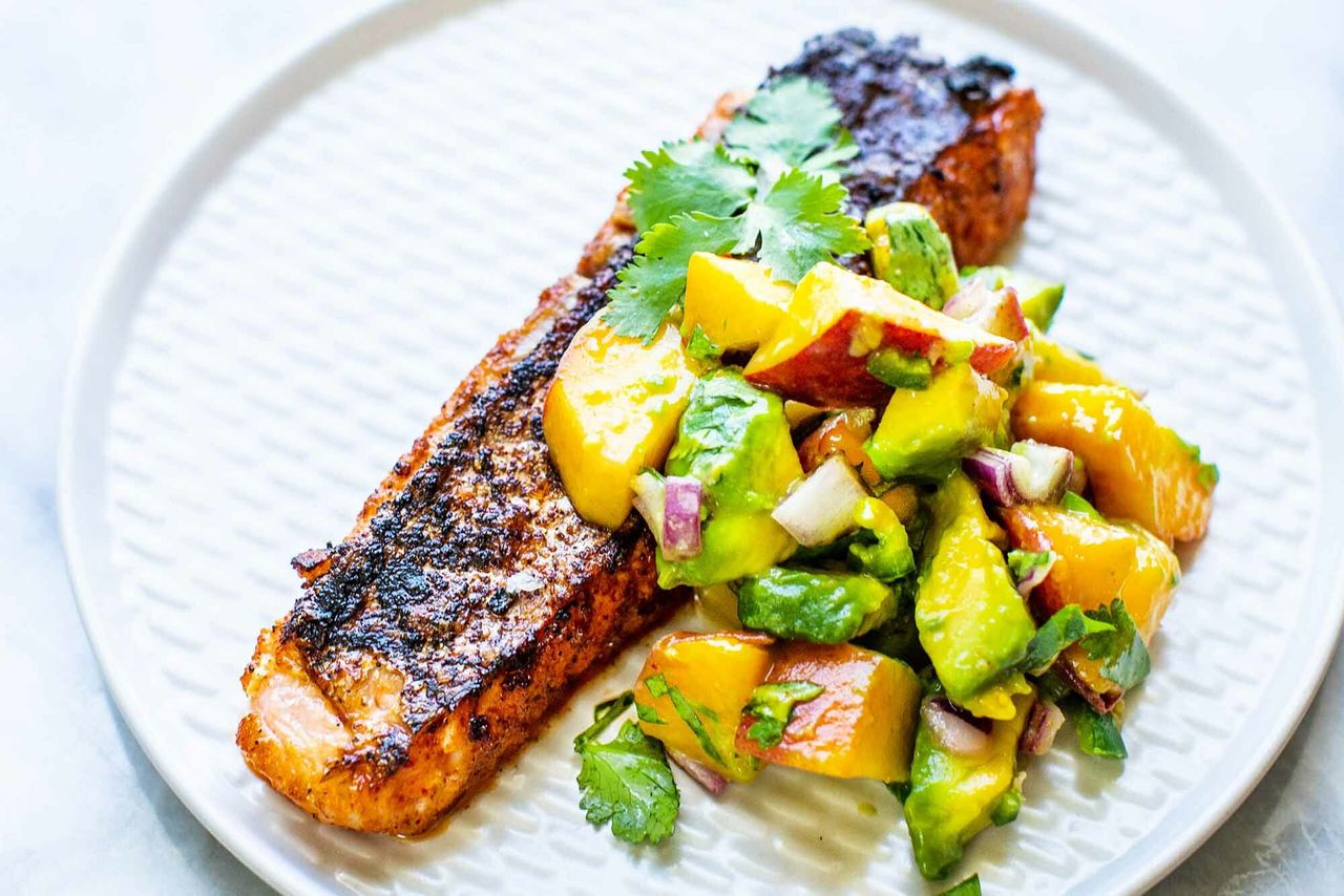 Grilled salmon fillet paired with a peach and avocado salsa served on a white plate