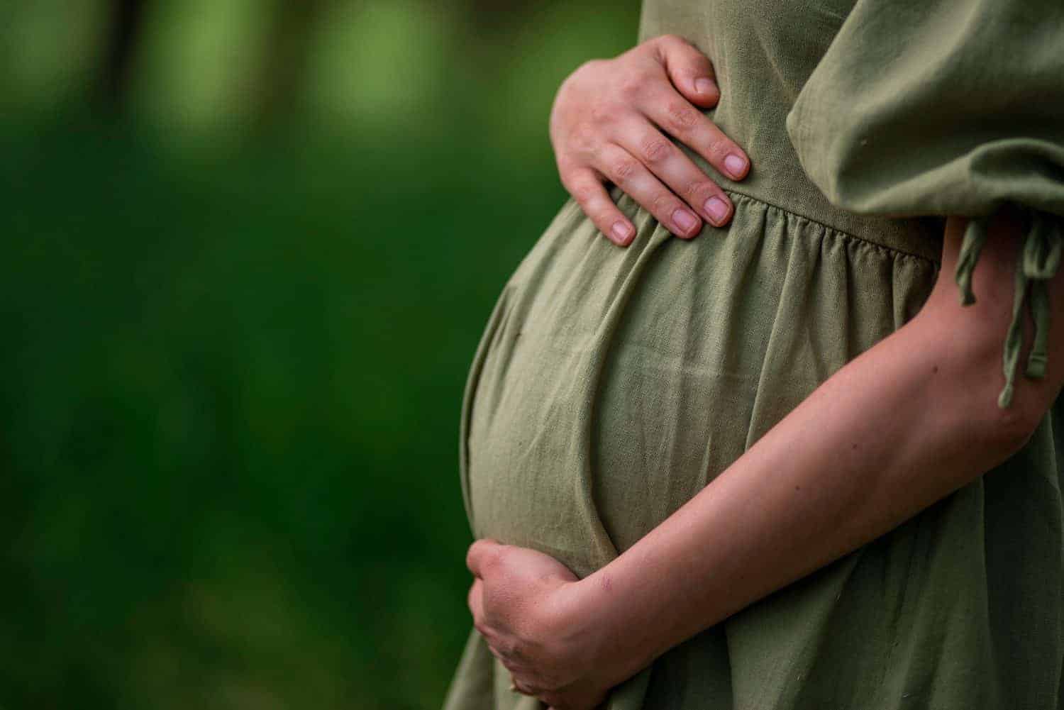 Caucasian Young Pregnant woman Tummy belly summer green dress touching stomach field expecting a baby relaxing outside nature park lake rural Beautiful magic 8 months enjoying life glasses hat