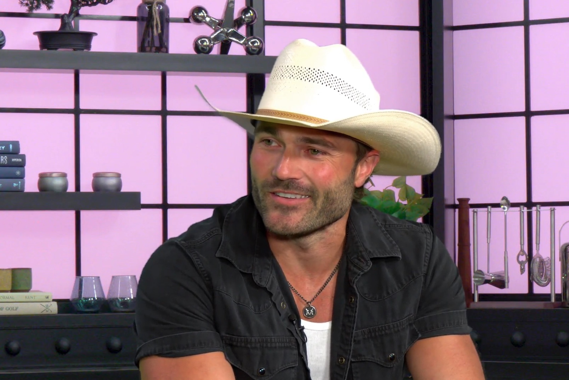 A man in a white cowboy hat and black shirt looks right, smiling.