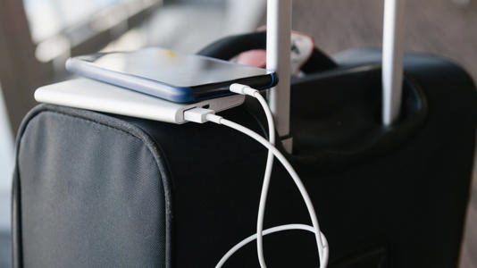 Smartphone plugged into a power bank and charging atop luggage.