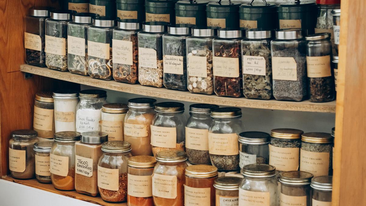 Different herbs and spices in labelled bottles on wooden shelving.