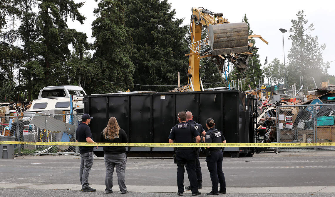 Richland code enforcement and police officers watch Monday morning as an excavator, operated by a local contractor hired by the city of Richland, begins cleanup and removal of junk, vehicles and debris from 2100 Pullen Street in Richland.