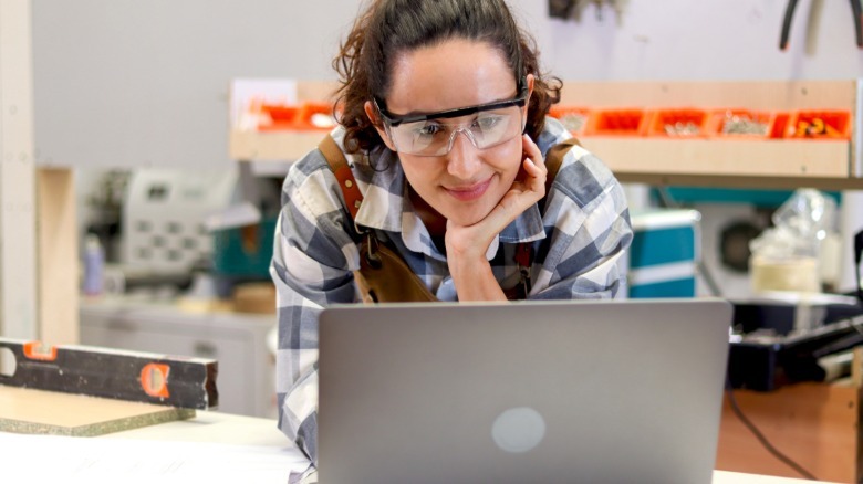 Smiling woman in workshop watching how-to video on laptop