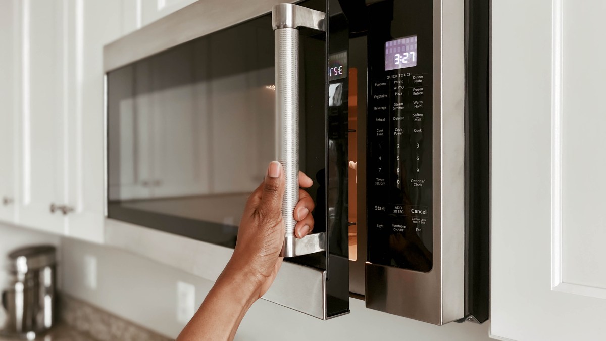 A hand opening a microwave door.