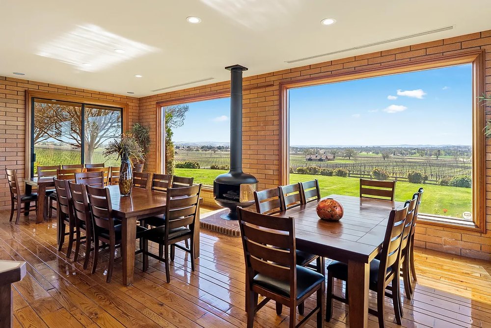 Bright dining room surrounded by picture windows, exposed brick accent walls, and a freestanding wood stove.
