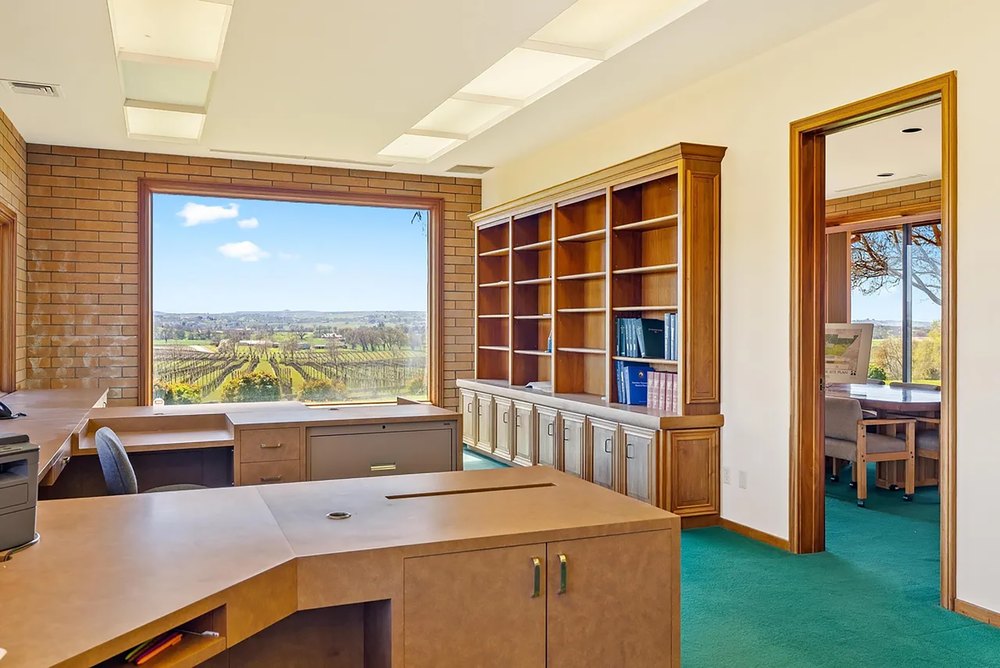 Spacious office area featuring custom built-in wooden bookshelves, desk workstations, and vineyard views.