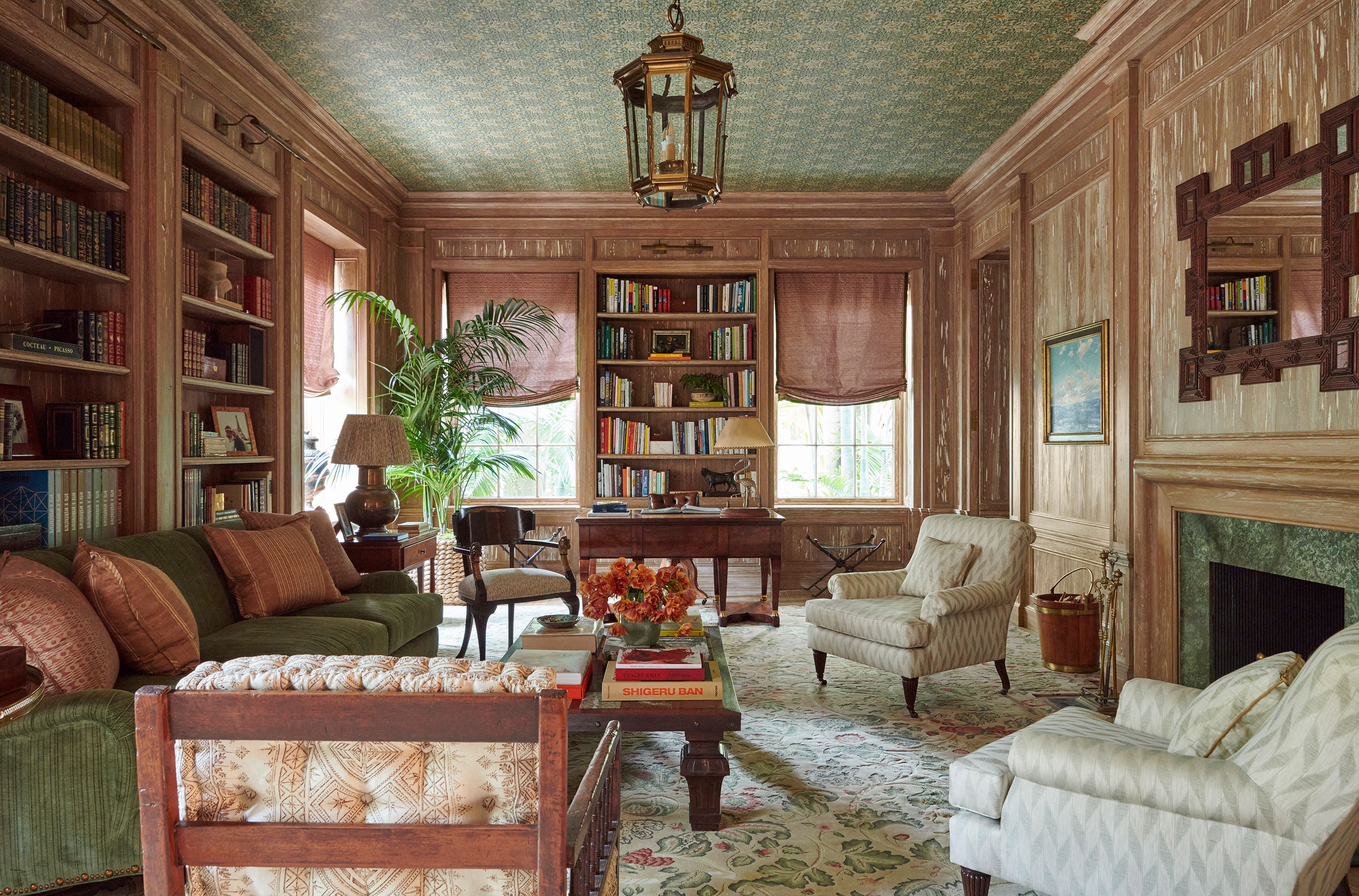 The library is where Graziolo could really flex her muscles. The devoted classicist borrowed details from the original stair railings in the foyer and repurposed them in the capitals of the columns in the room. A carpet from Rug and Kilim and wallpaper from Morris & Company enliven the floor and ceiling. The moss green of the custom sofa picks up the green of the room’s mantel, while picture lights from Chelsea Textiles illuminate the shelves, and an antique desk anchors one end of the room. The club chairs are upholstered in a Rose Tarlow fabric, and the Roman shades are done in a Fortuny pink.