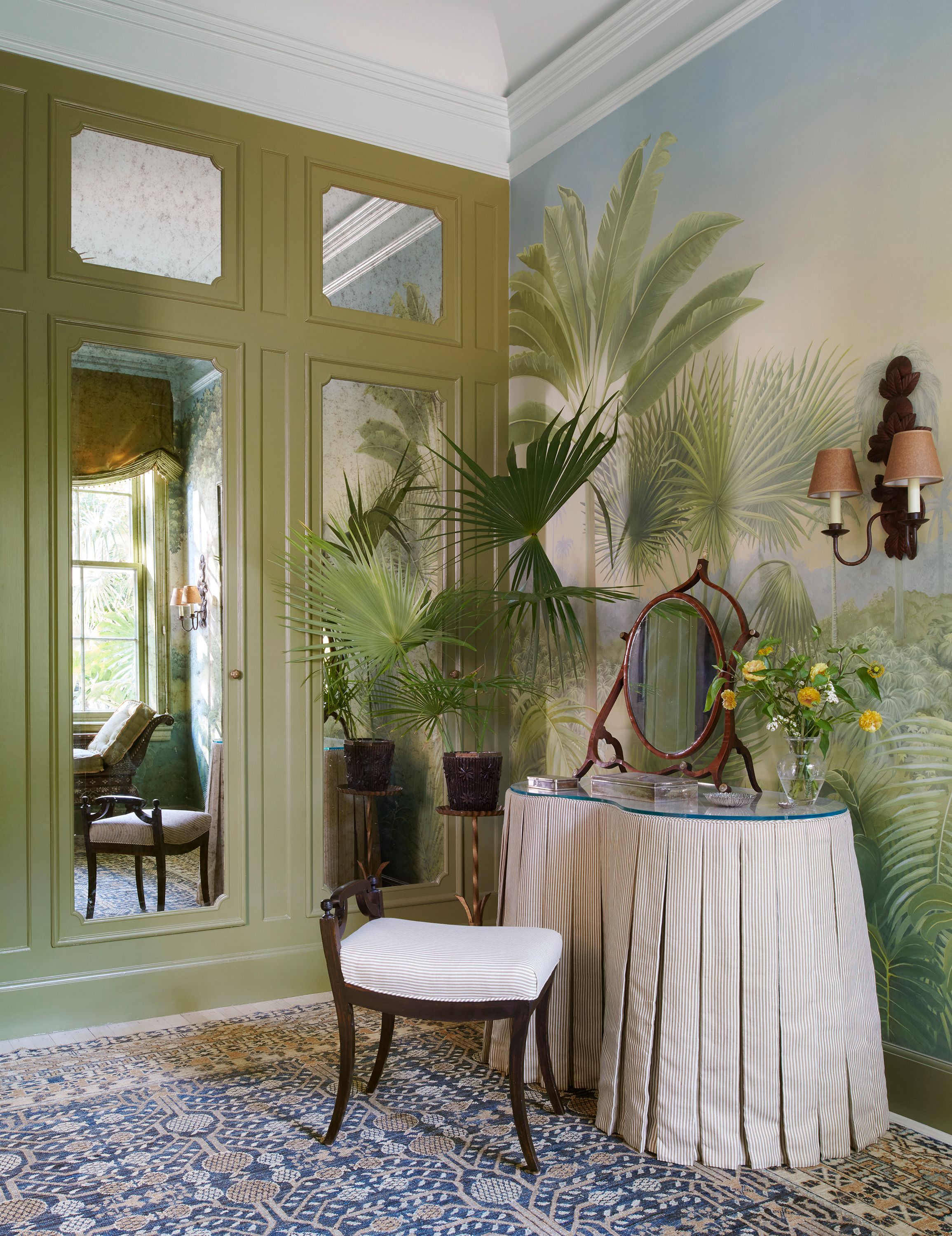 Agustin Hurtado painted a tropical mural inspired by the house’s surrounding foliage in the ladies dressing room. An antique daybed hovers under one window, while the same muted stripe that hugs the kidney-shaped vanity also covers the stool in front of it. The rug is from Marc Philips.
